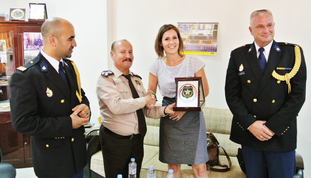 Four adults in formal uniforms presenting and receiving an award plaque in an office setting.