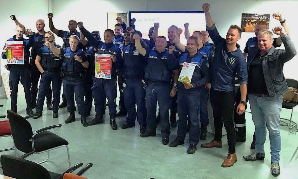 Group of uniformed emergency responders standing in a room, fists raised in celebration, with a few holding posters.