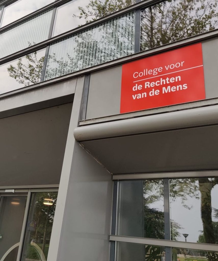 Red sign reading 'college voor de Rechten van de Mens' on a modern building exterior.
