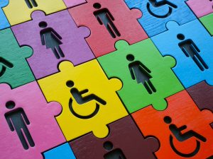 Colorful interlocking puzzle pieces with silhouettes of people (including a wheelchair symbol) symbolizing inclusion and accessibility.