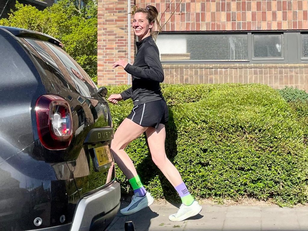 Woman in black athletic outfit smiling as she steps out of a dark SUV onto a sidewalk, wearing neon green socks and lavender legwear.
