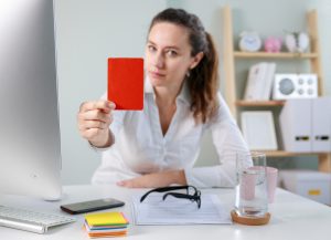 Woman at a desk holding up a red card toward a computer monitor in an office setting.