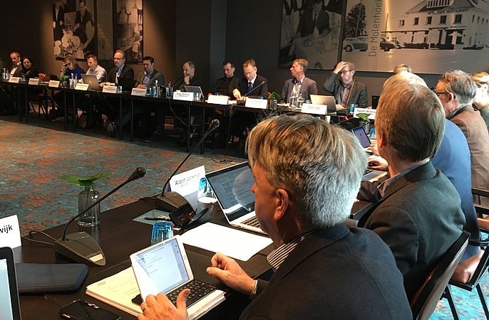 Group of professionals at a conference table with laptops and microphones during a meeting.