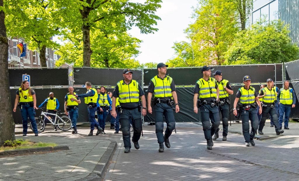 Samen aan het werk - Nederlandse Politiebond Line of police officers in high-visibility vests walking down a tree-lined street, with bicycles nearby and construction barriers behind them